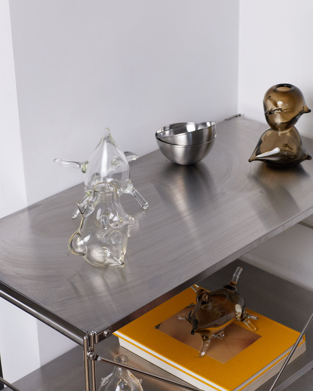 Metallic sculptures and a bowl on a reflective surface with a white background