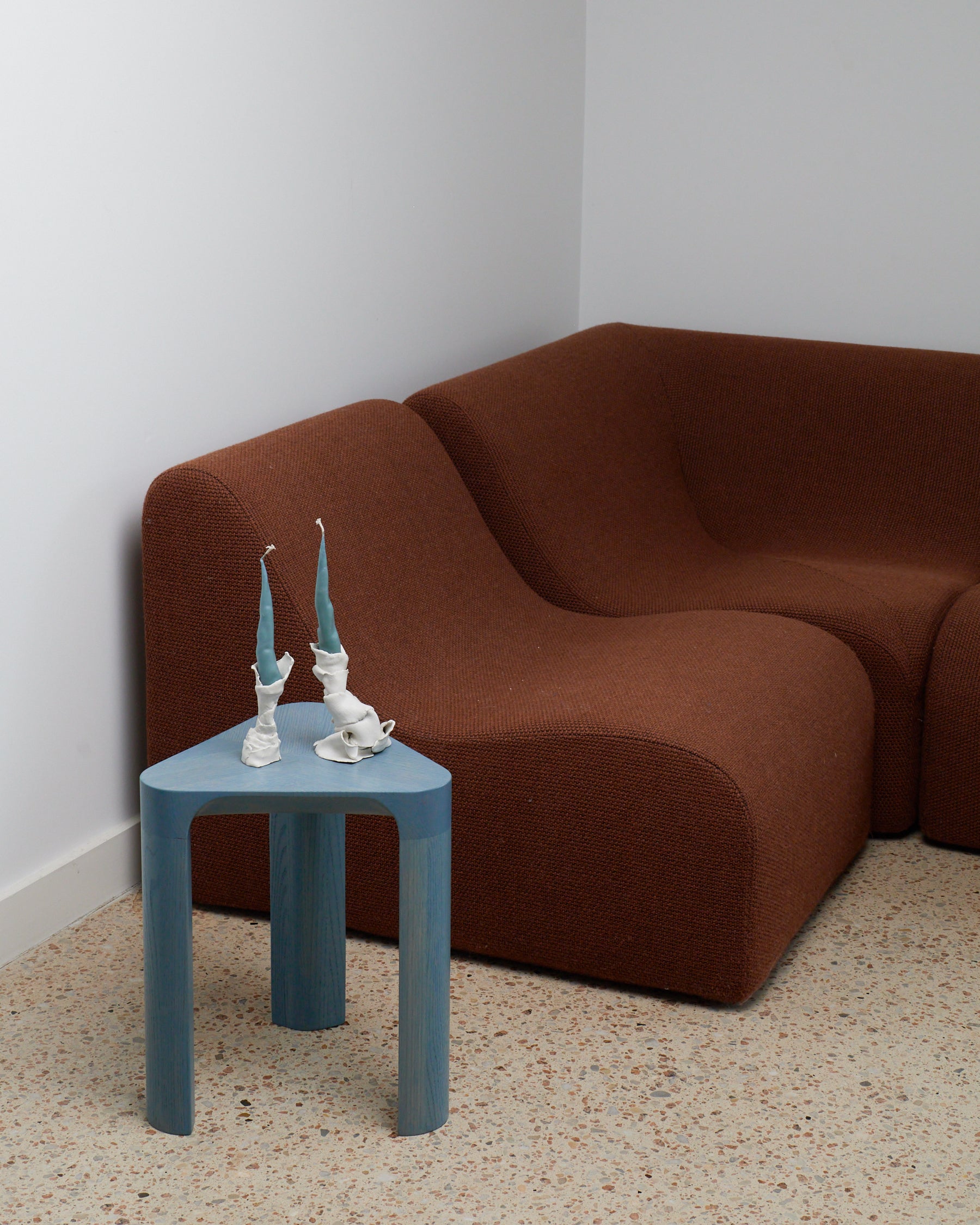 Blue side table with decorative items in front of a brown sofa against a white wall.