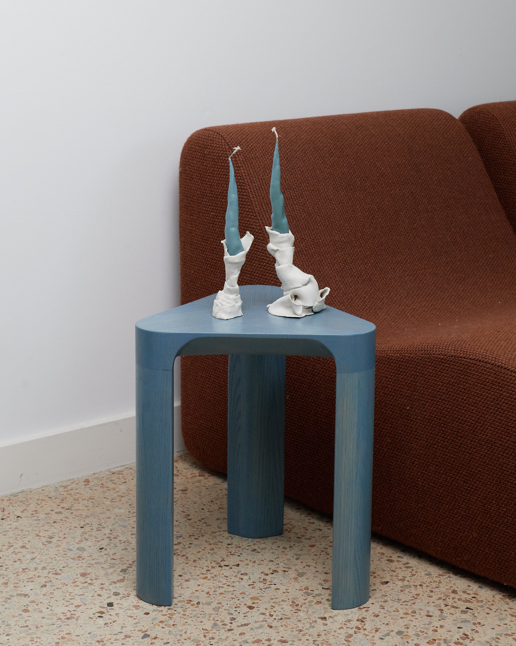 Blue side table with decorative items against a brown sofa and white wall.
