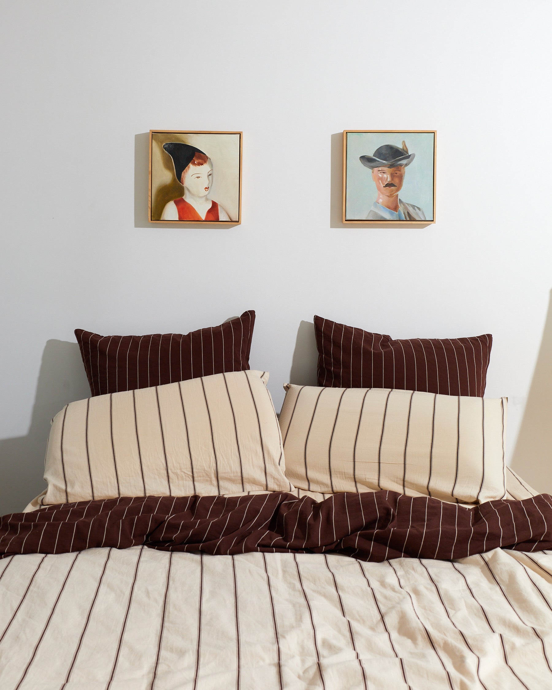 Beige and brown striped bedding with pillows, framed portraits on the wall.