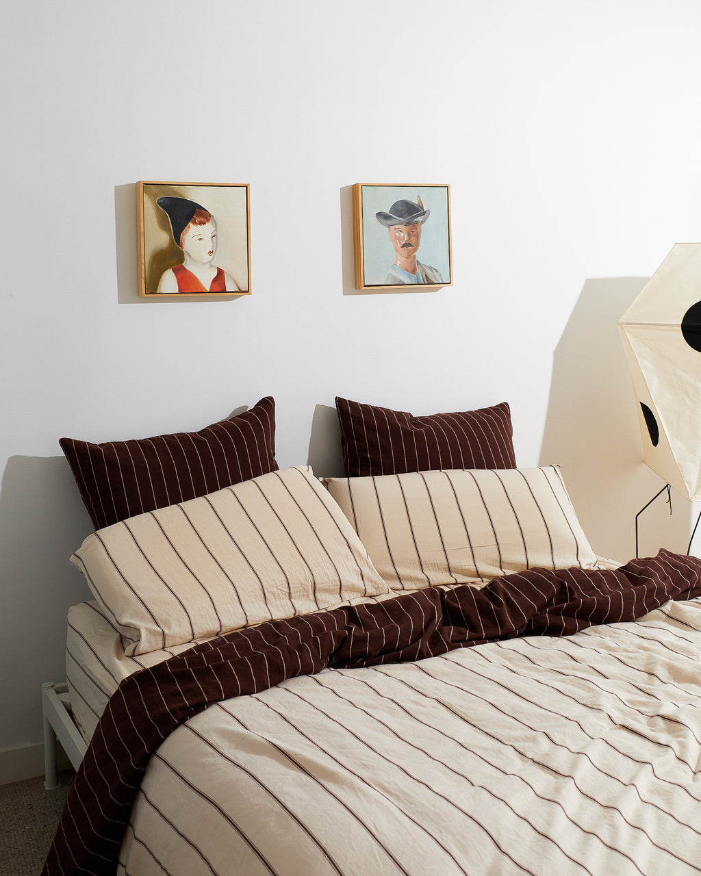 Bed with striped bedding and pillows in a room with framed pictures on the wall.