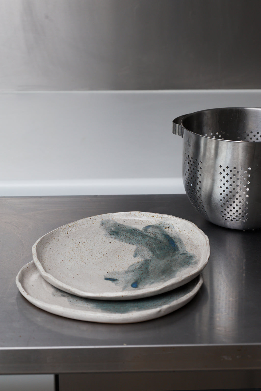 Two ceramic plates with blue abstract designs on a dark surface, with a metal colander in the background.