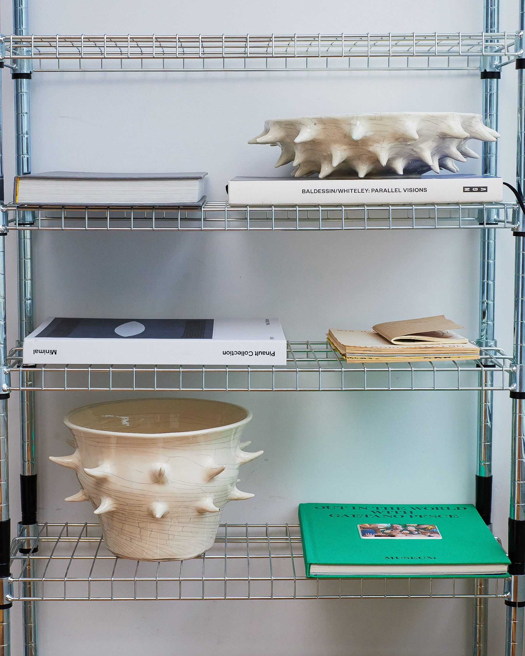 Metal shelving unit with books and a ceramic pot on a white background