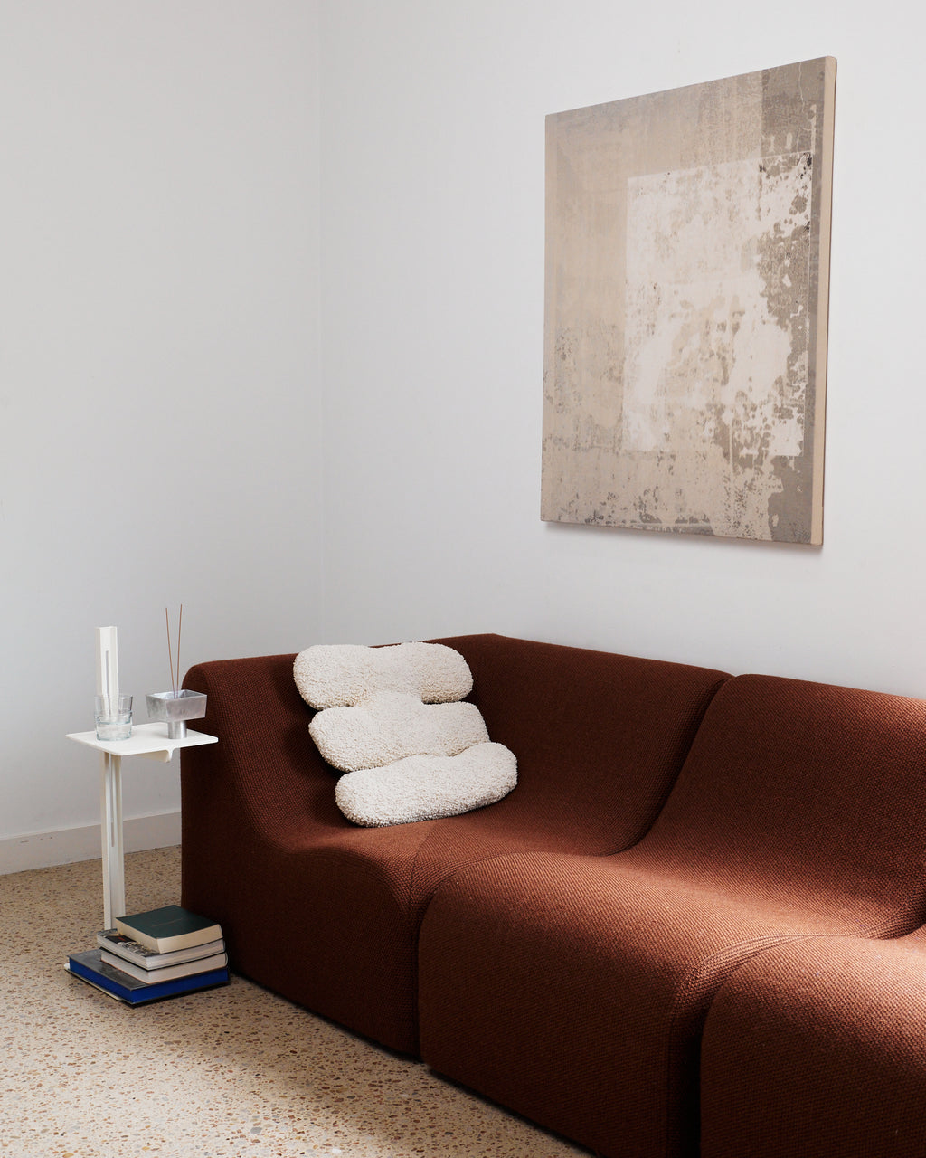 Brown sofa with white cushions in a room with a abstract painting on the wall.
