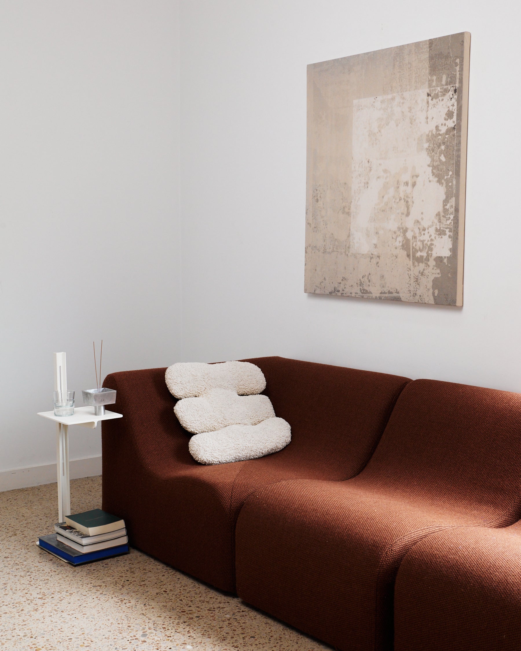 Brown sofa with white cushions in a room with a abstract painting on the wall.