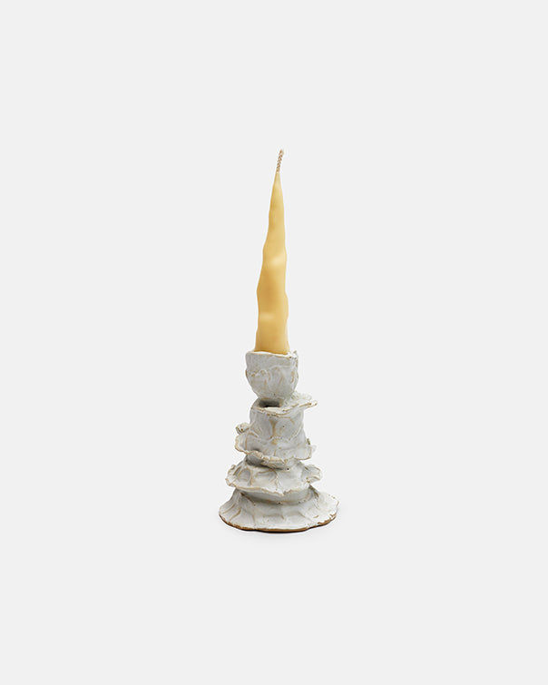 White ceramic candle holder with a lit yellow candle on a white background