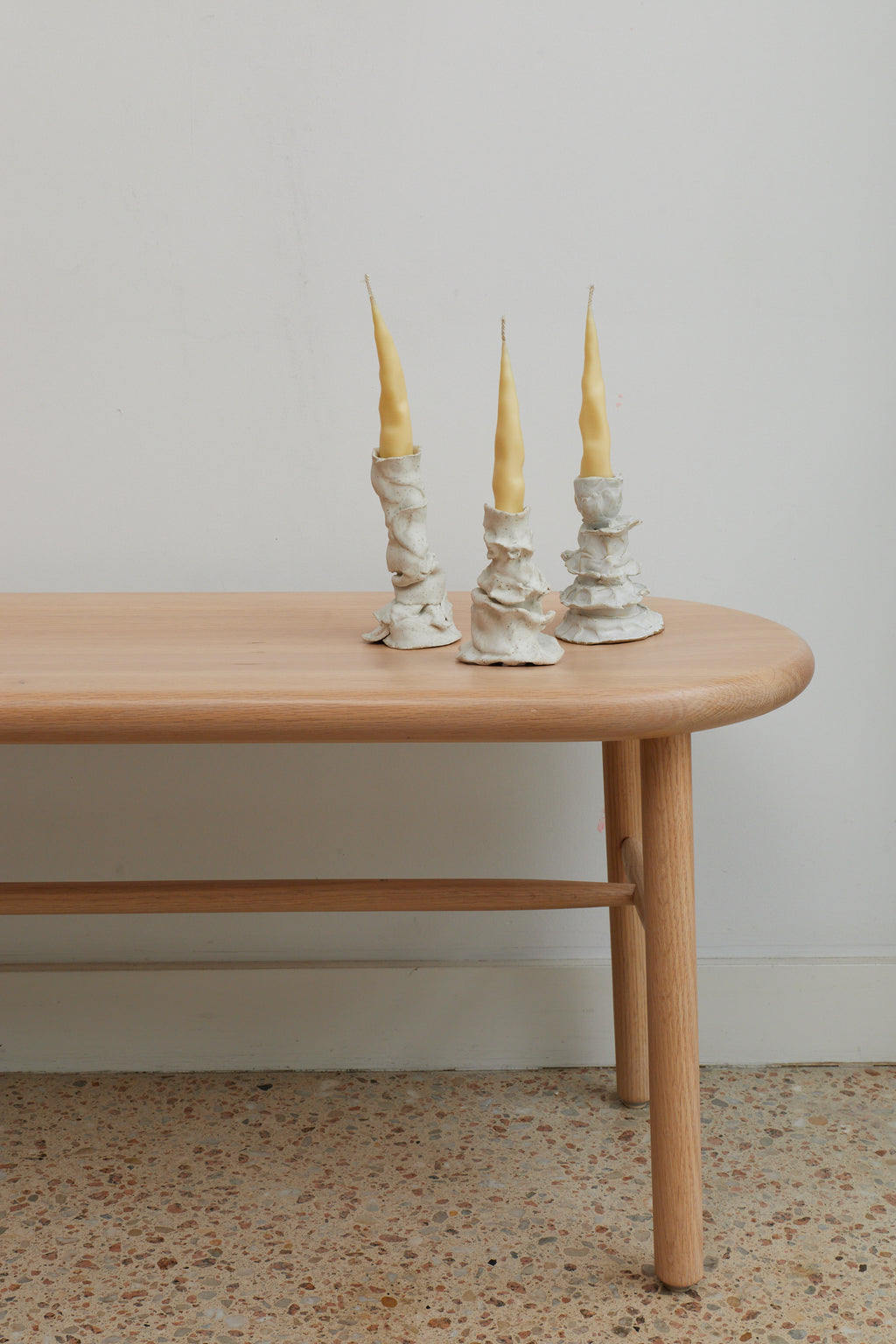 Three candlesticks with yellow candles on a wooden table against a plain wall.