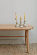 Three candlesticks with yellow candles on a wooden table against a plain wall.
