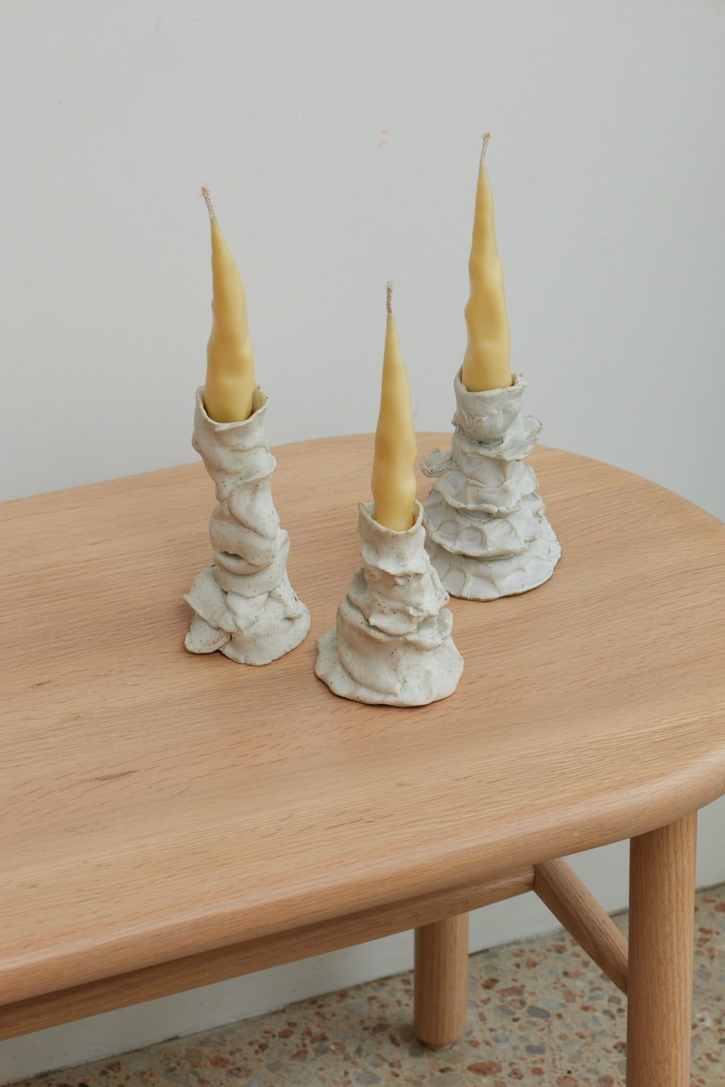 Three candlesticks with yellow candles on a wooden table against a plain wall.