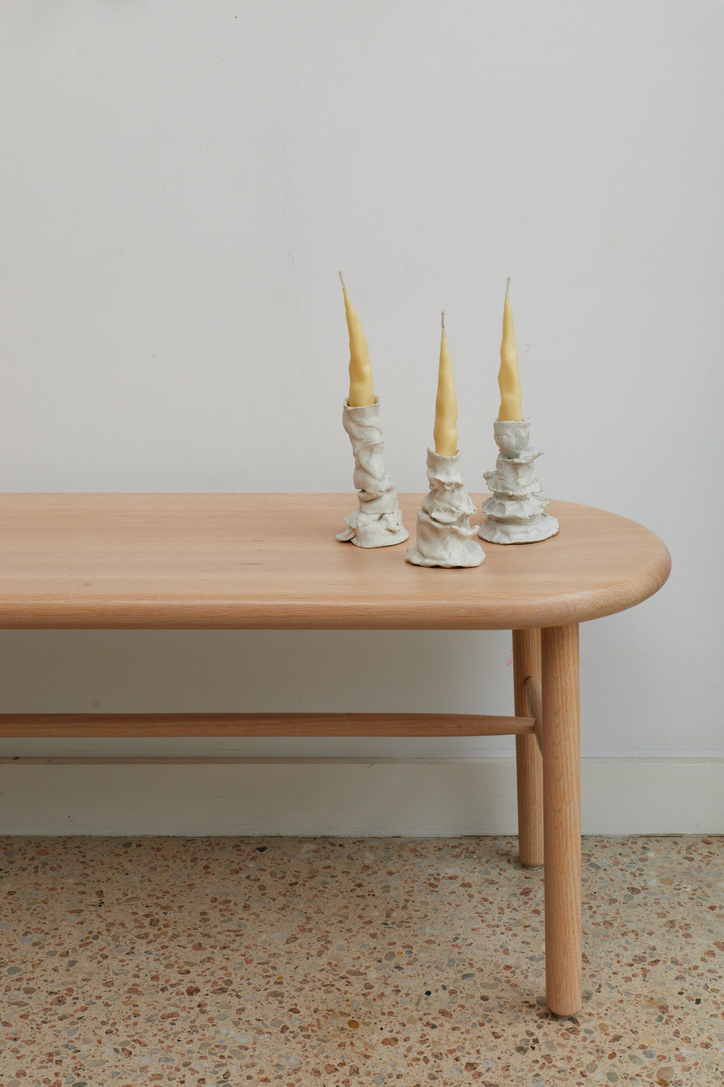 Three decorative candle holders with yellow candles on a wooden table against a plain wall.