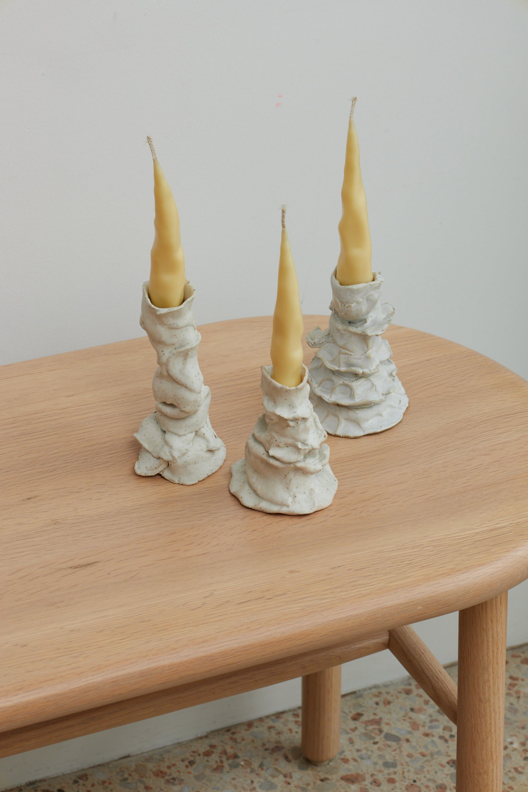 Three tall, pointed candles in decorative holders on a wooden table.