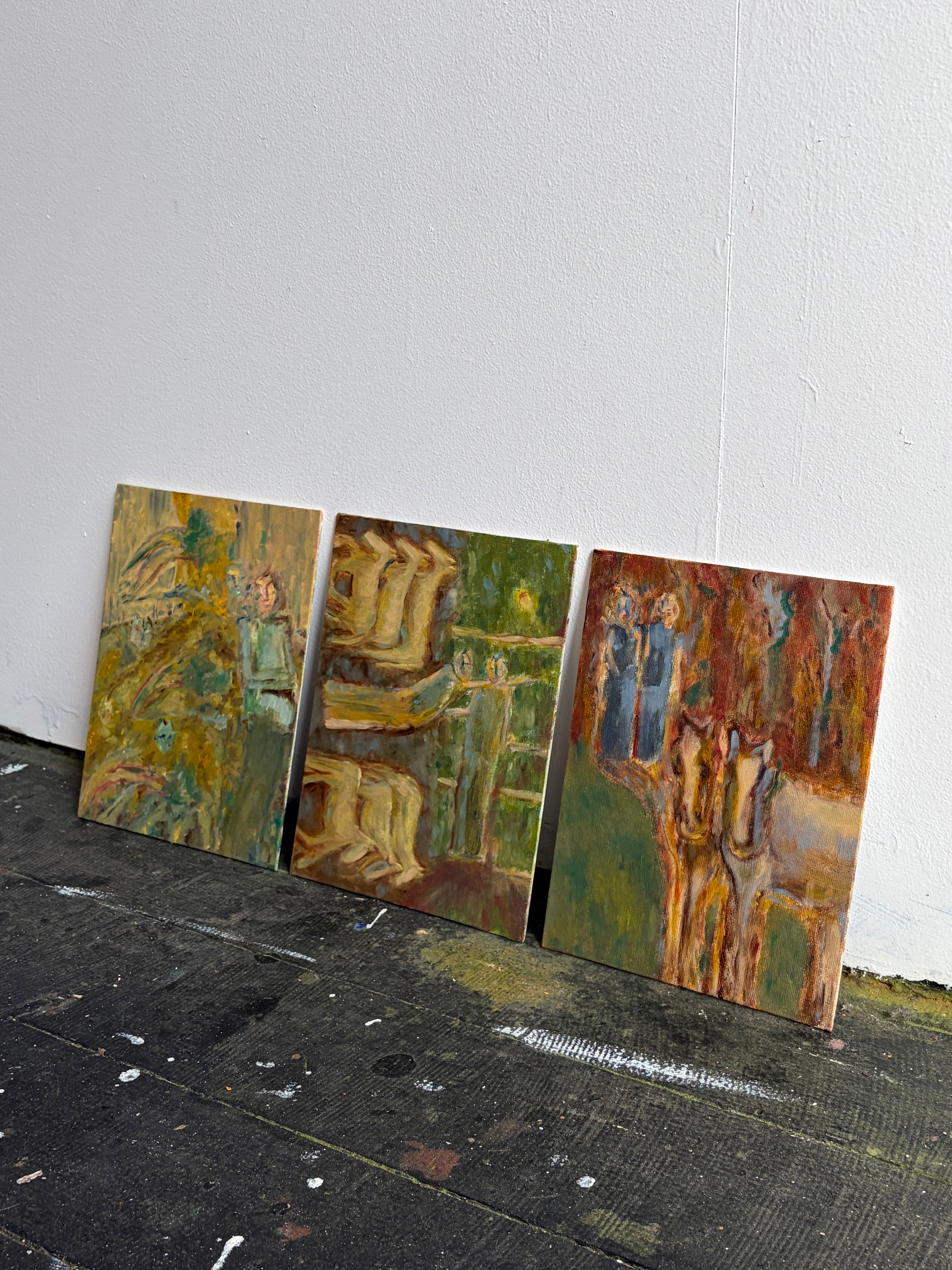Three abstract paintings leaning against a white wall on a black floor.
