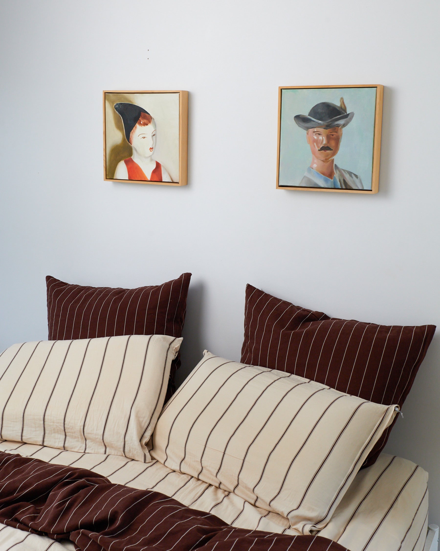 Bed with striped bedding and pillows, framed portraits on the wall.