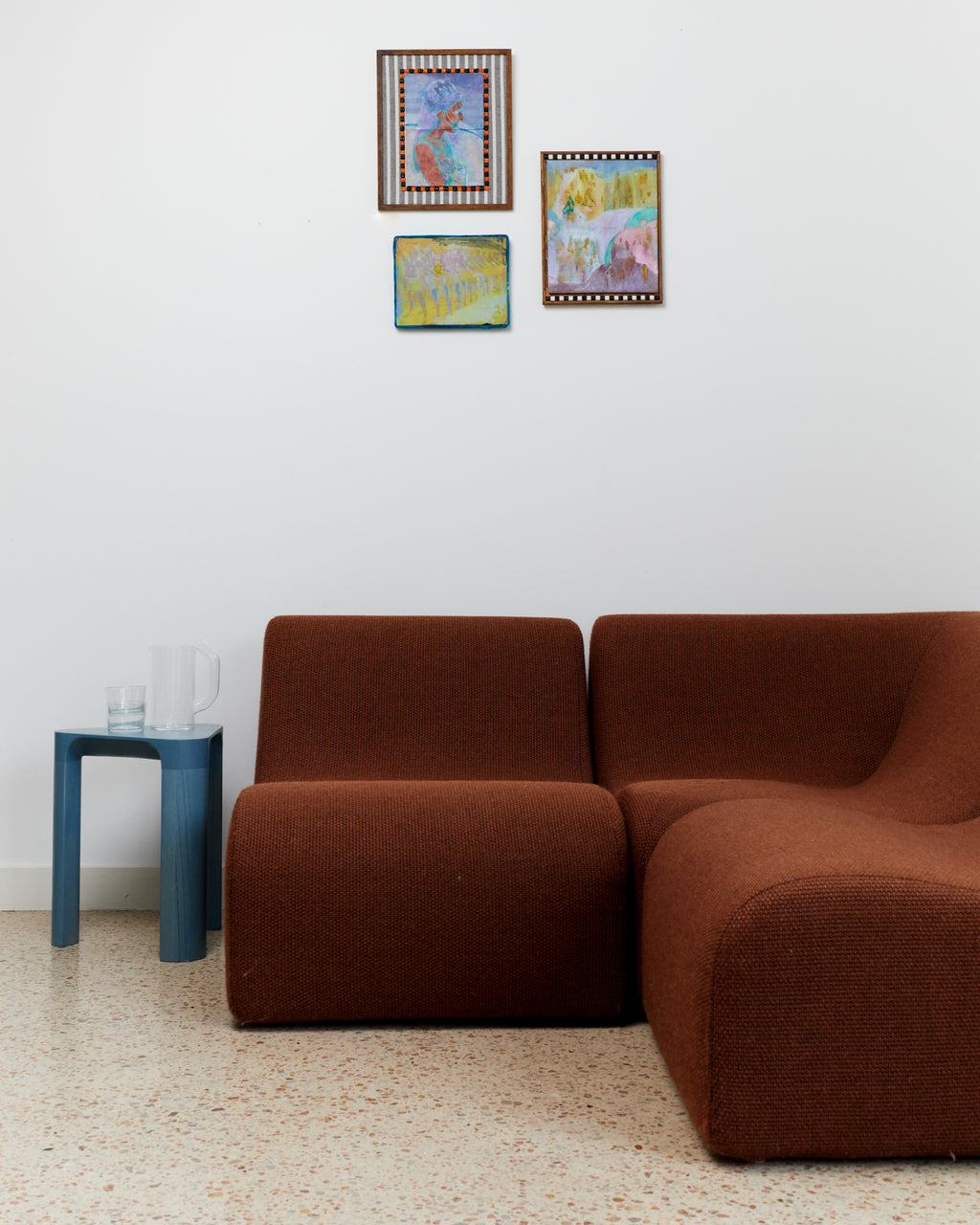 Brown sofa in a room with three colorful paintings on the wall.