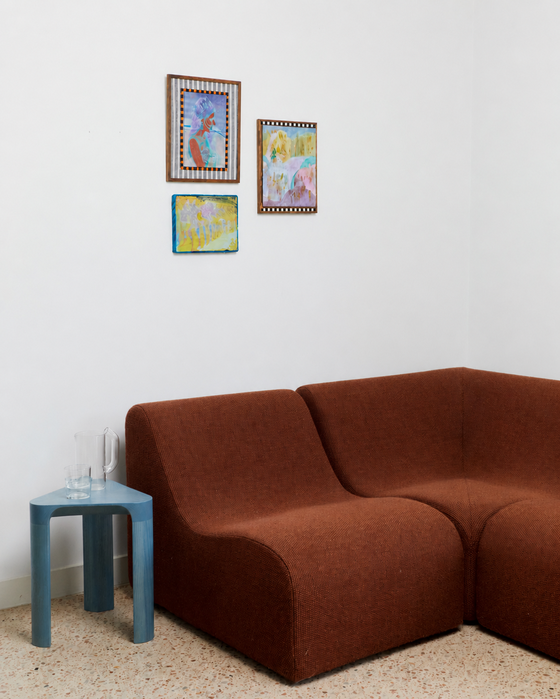 Brown sofa in a room with a blue side table and framed pictures on the wall.