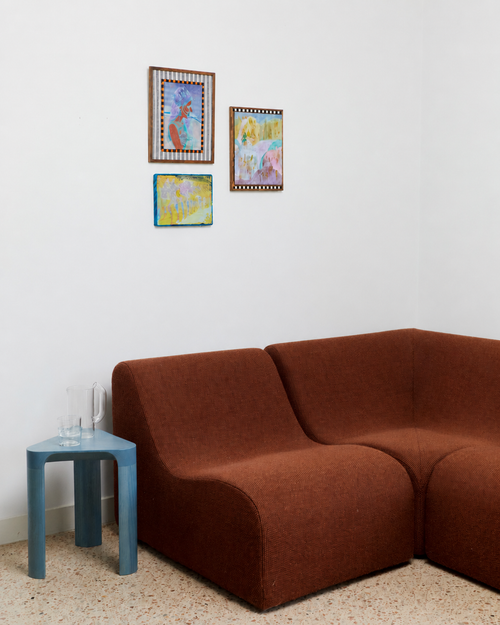 Brown sofa in a room with a blue side table and framed pictures on the wall.