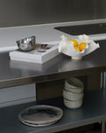 Stainless steel kitchen counter with bowls, a book, and a fruit bowl.