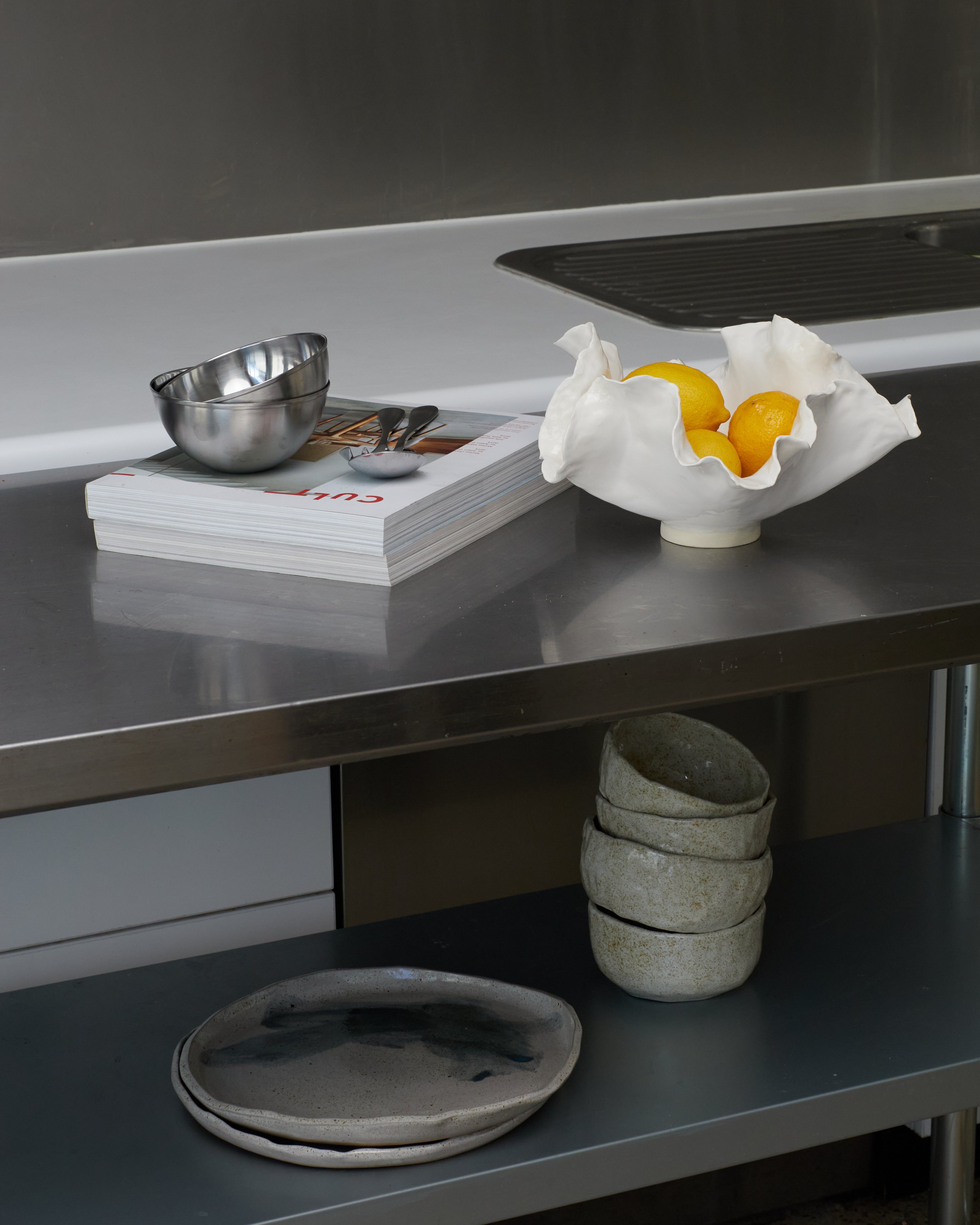 Stainless steel kitchen counter with bowls, a book, and a fruit bowl.