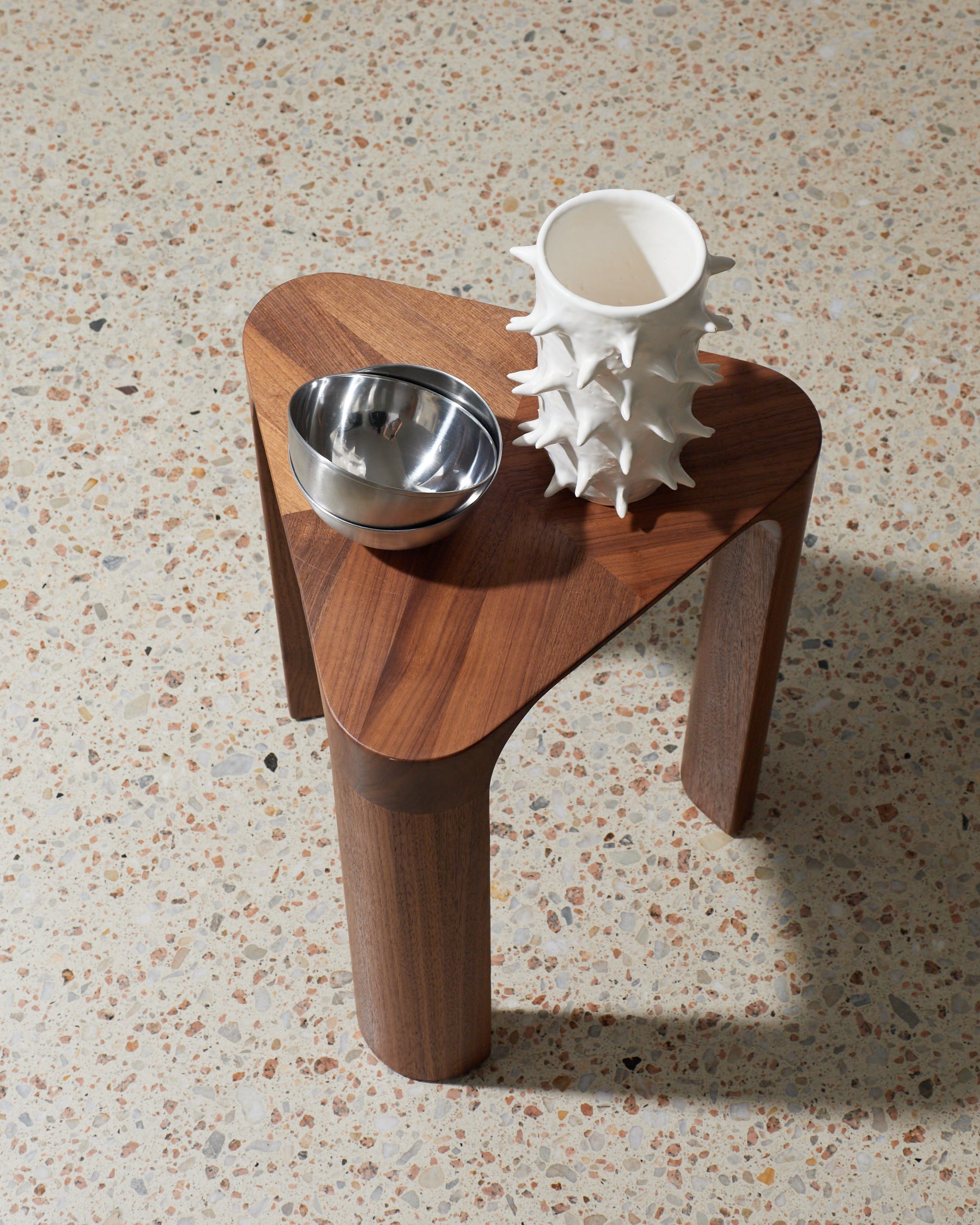 Wooden side table with a metal bowl and a white textured vase on a speckled surface