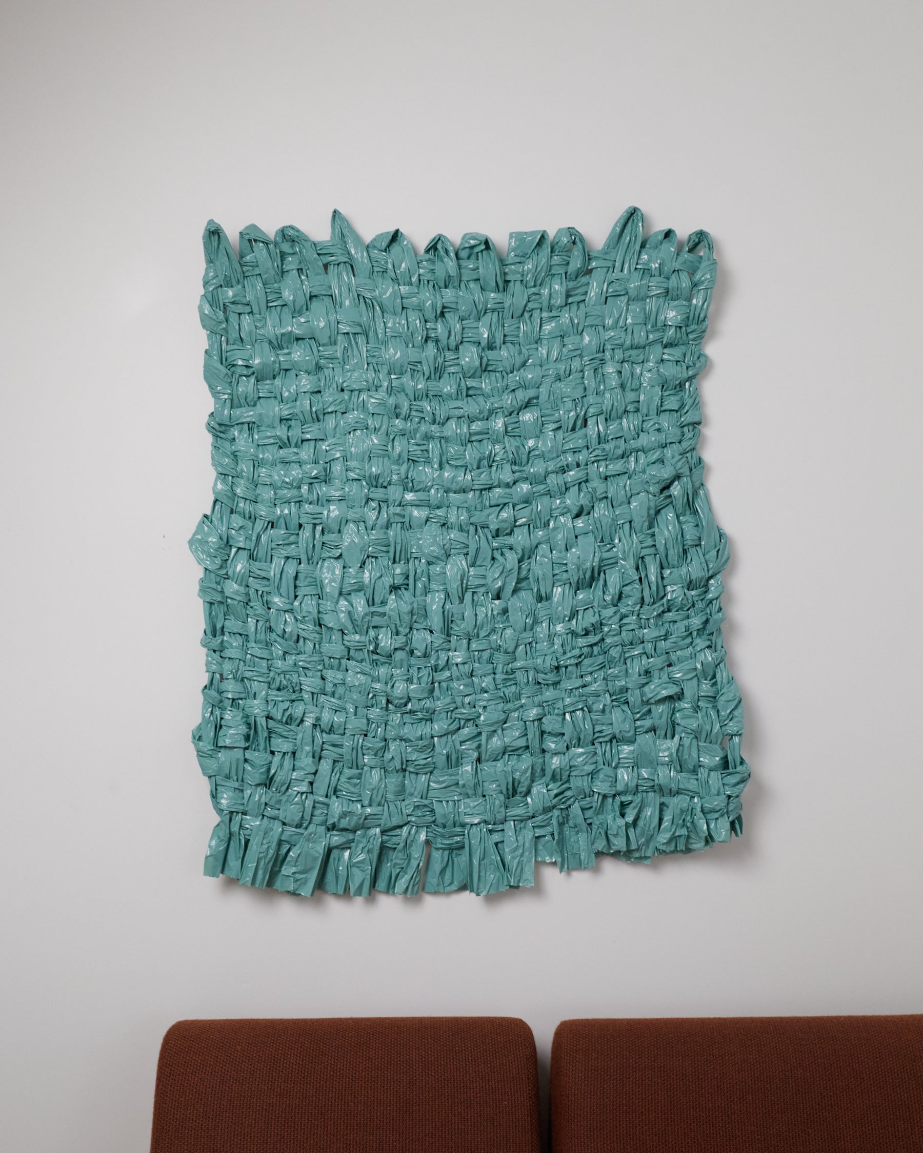 Teal textured rug on a plain white wall with brown furniture at the bottom.