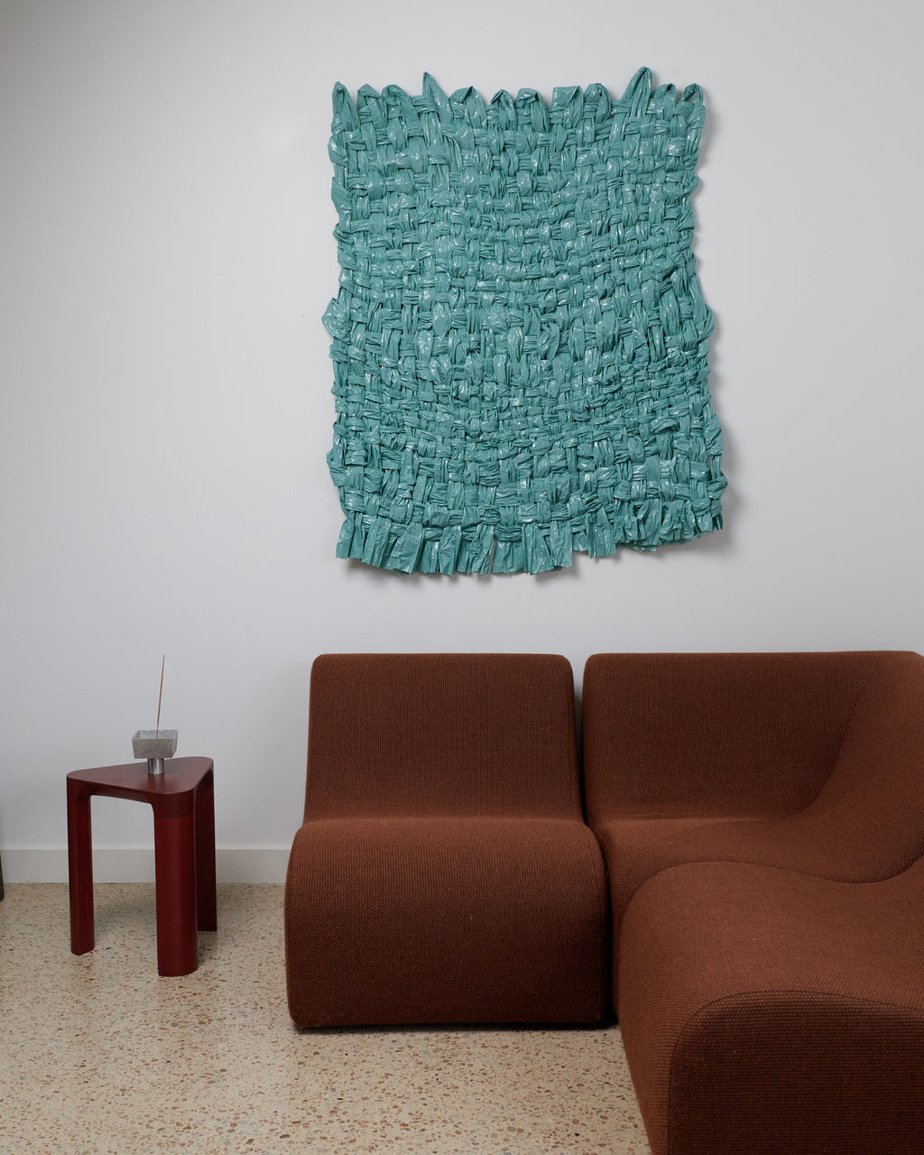 Turquoise textured wall art above a brown sofa in a minimalistic room.