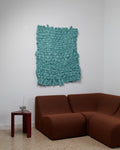 Turquoise textured wall art above a brown sofa in a room with a white wall.