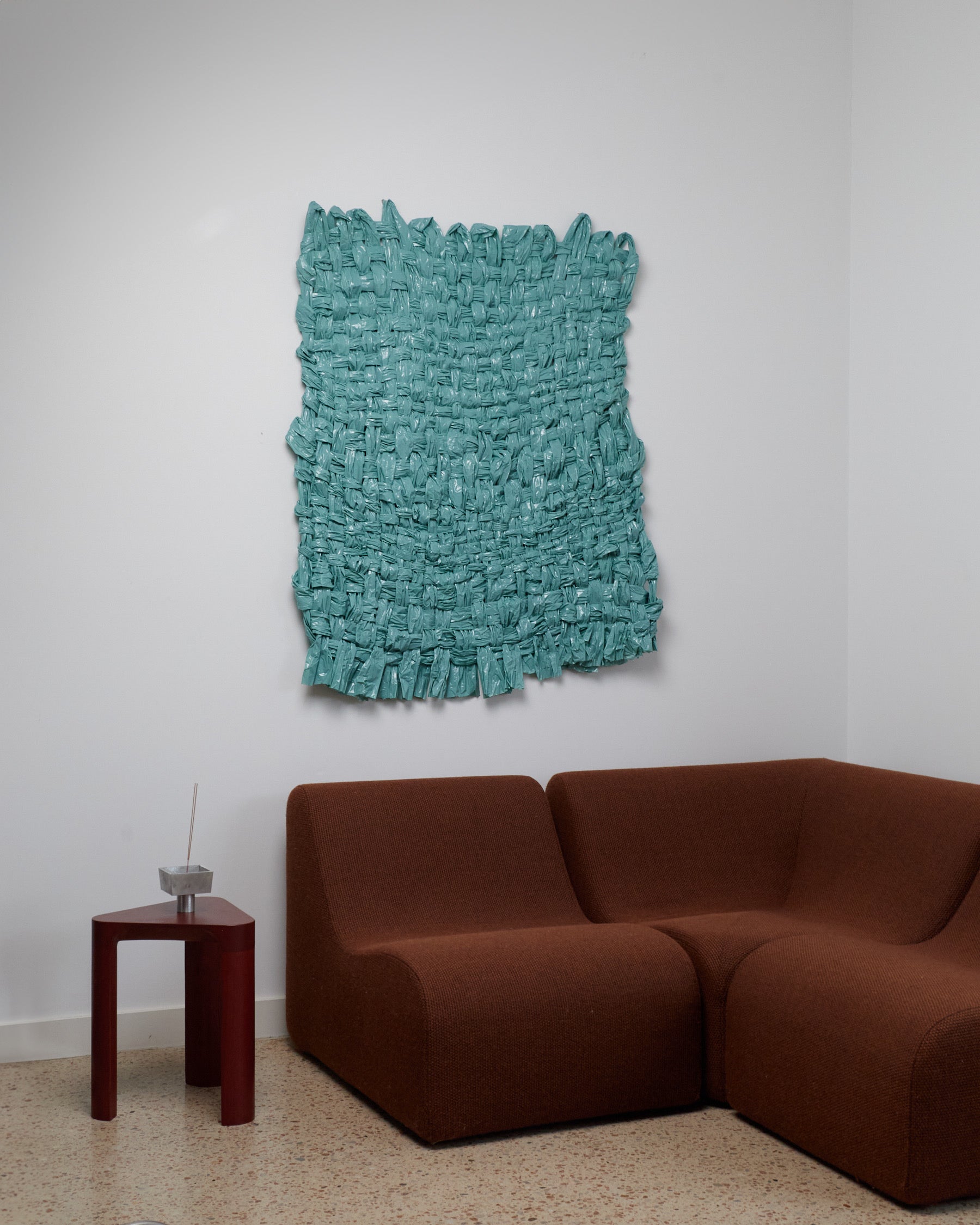 Turquoise textured wall art above a brown sofa in a room with a white wall.