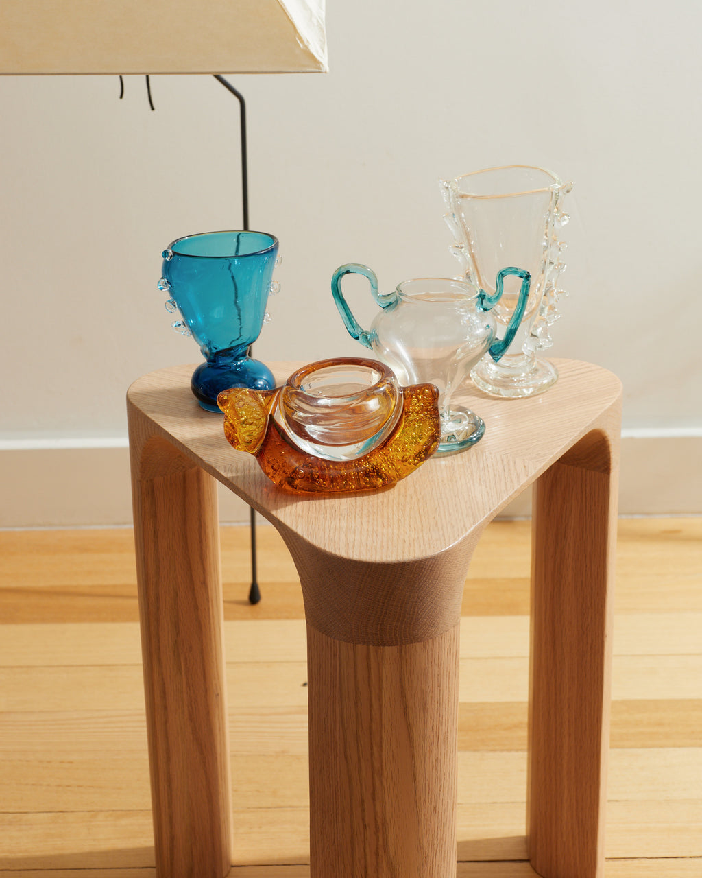 Wooden side table with colorful glassware on a wooden floor.