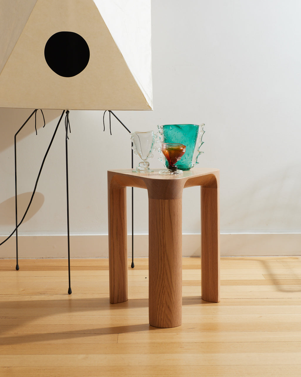Wooden side table with decorative items next to a lamp on a light wooden floor.