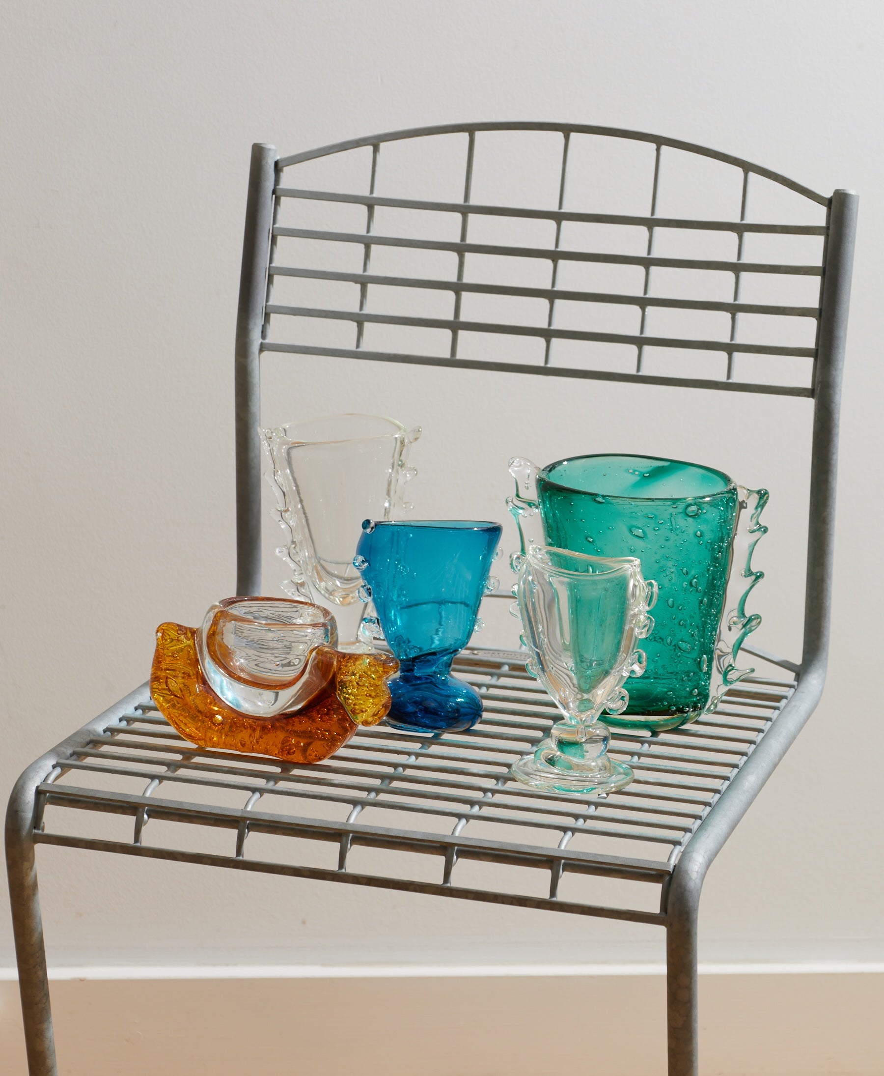 Colorful glassware on a metal shelf against a plain wall