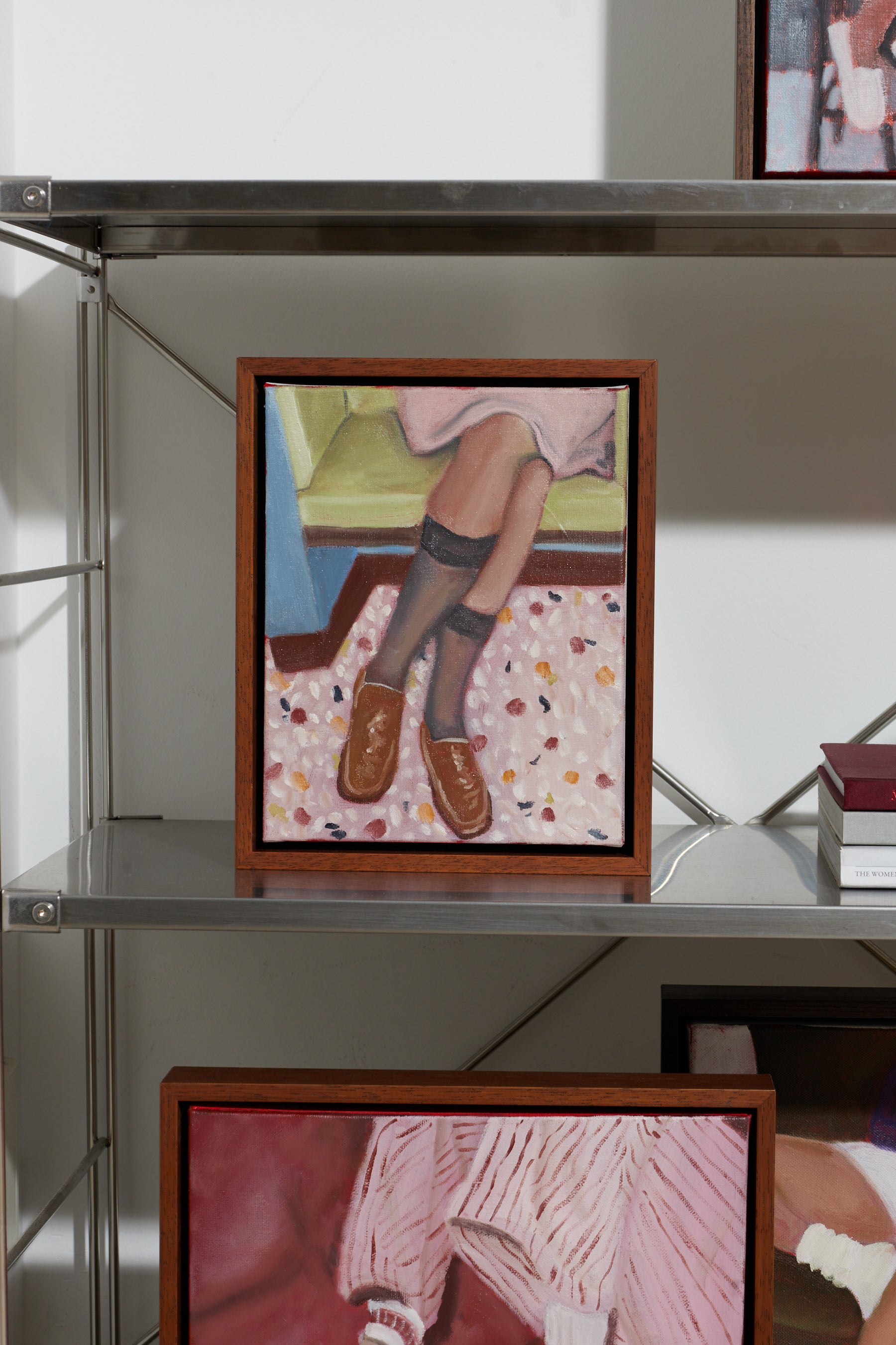Framed artwork of a person's legs on a shelf with other framed pieces.