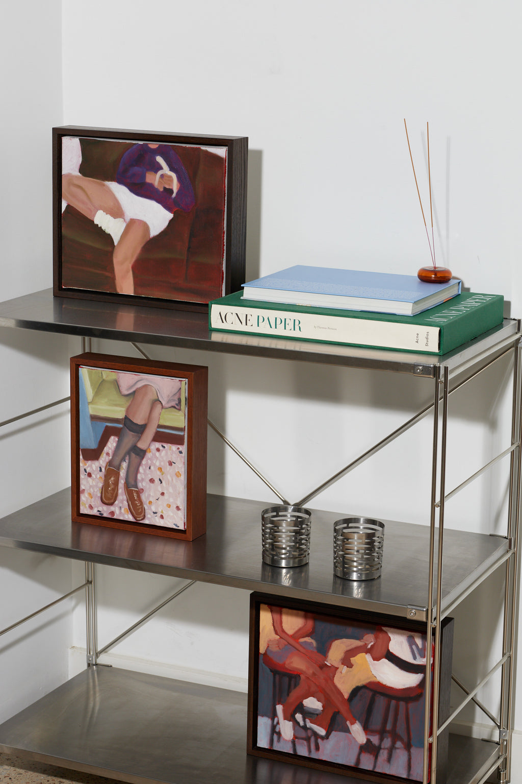 Metal shelf with books, a plant, and framed pictures on a white wall background