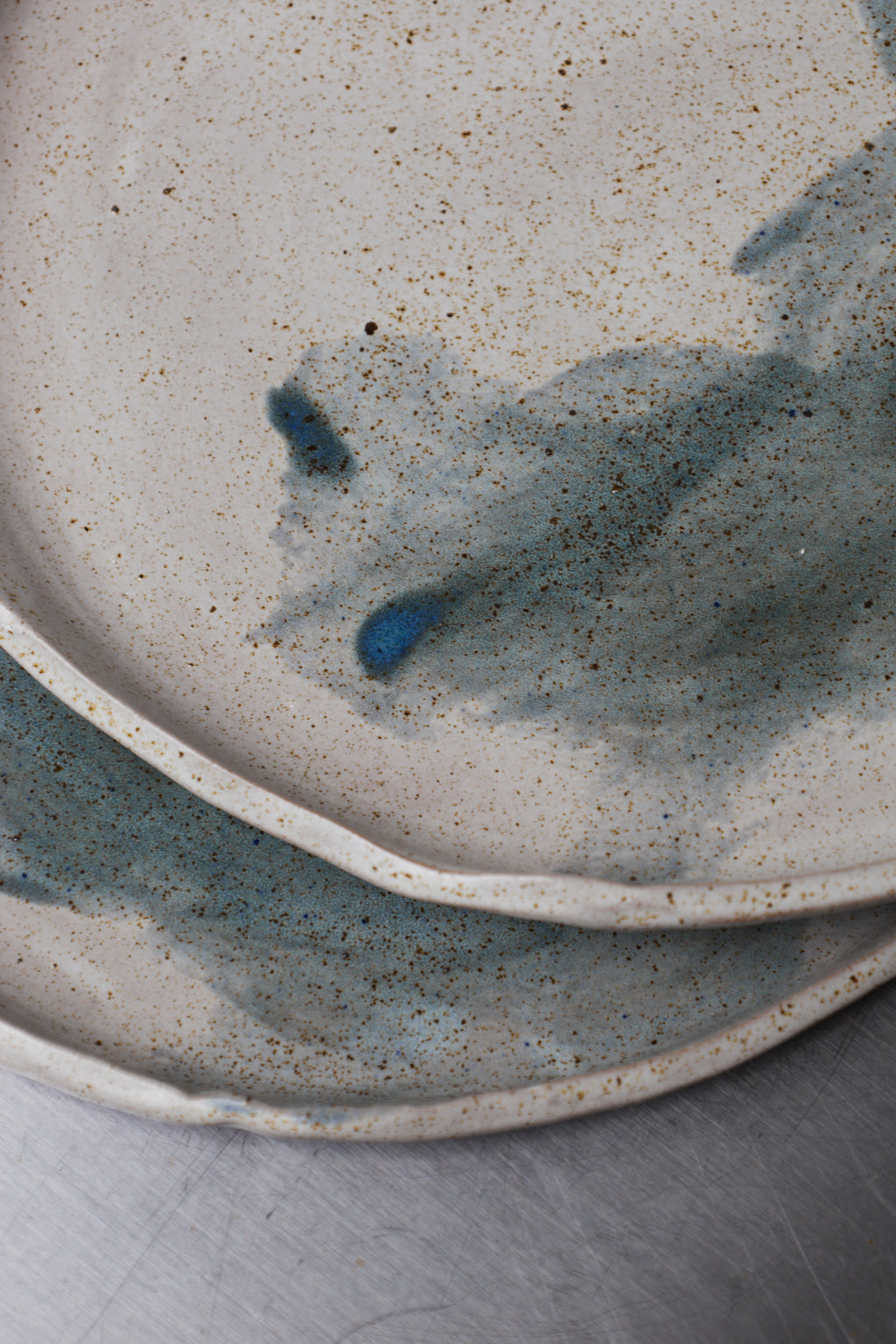 Two ceramic plates with a speckled glaze pattern on a neutral background
