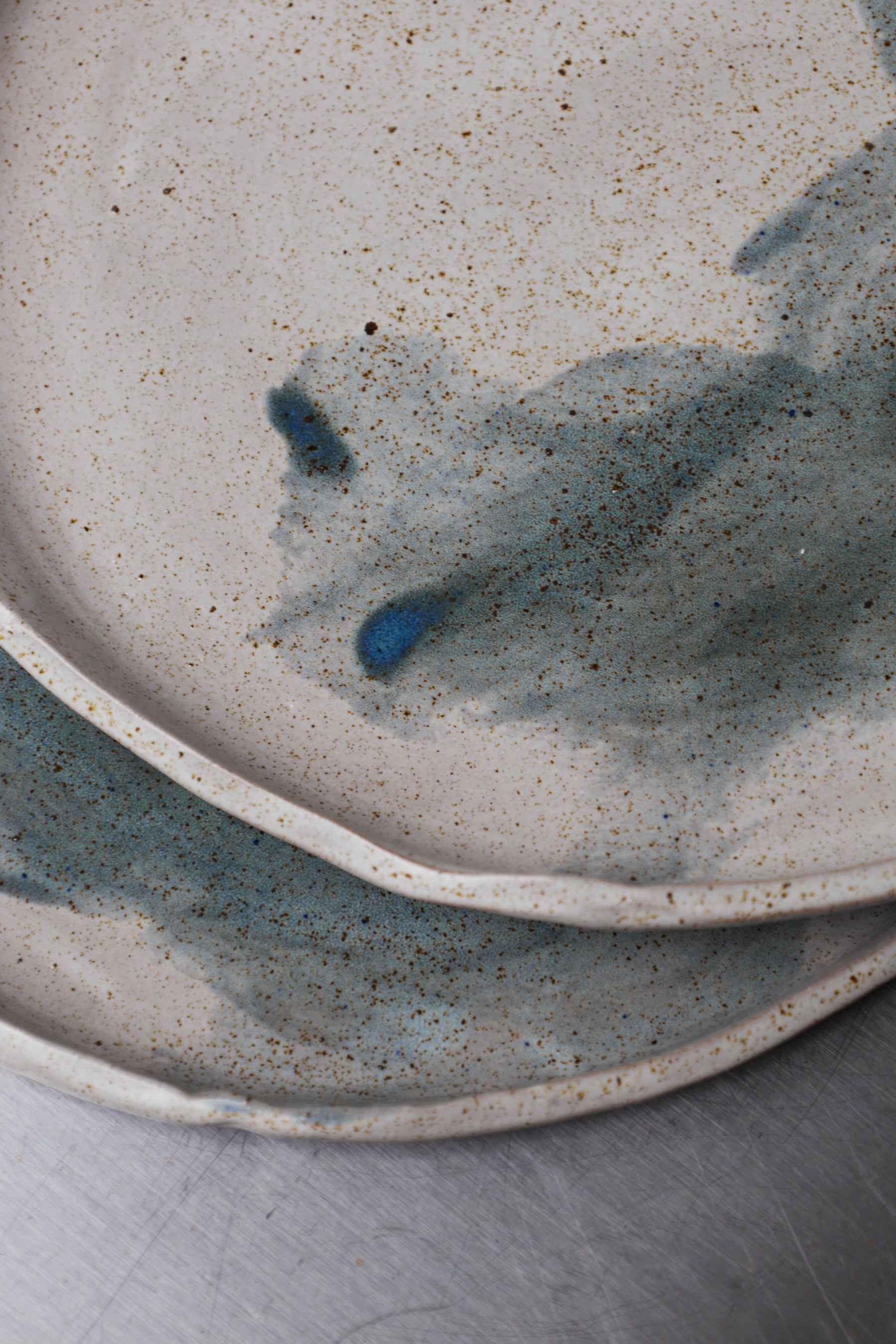 Two ceramic plates with a speckled glaze pattern on a neutral background