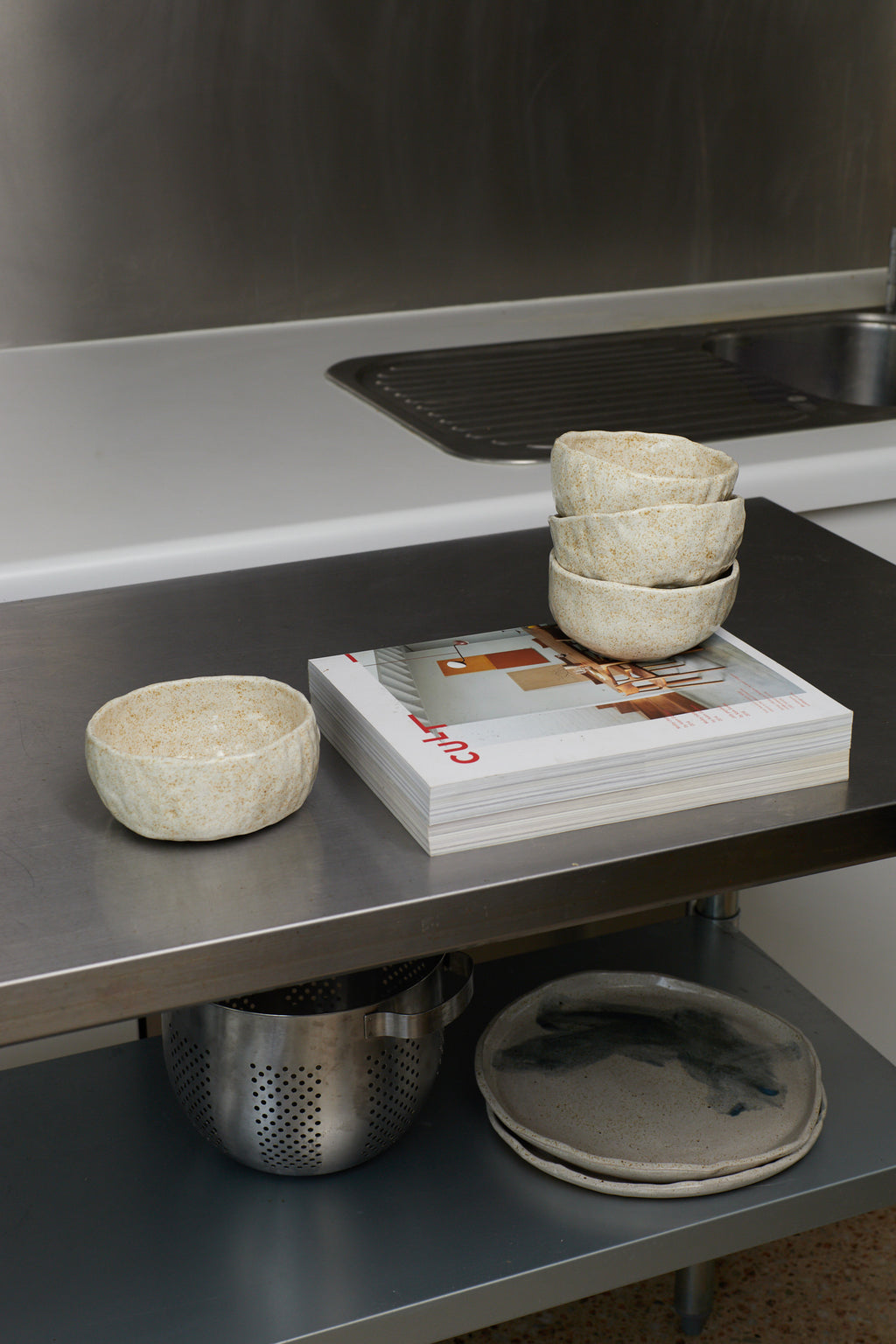 Kitchen counter with bowls, a magazine, and a colander.