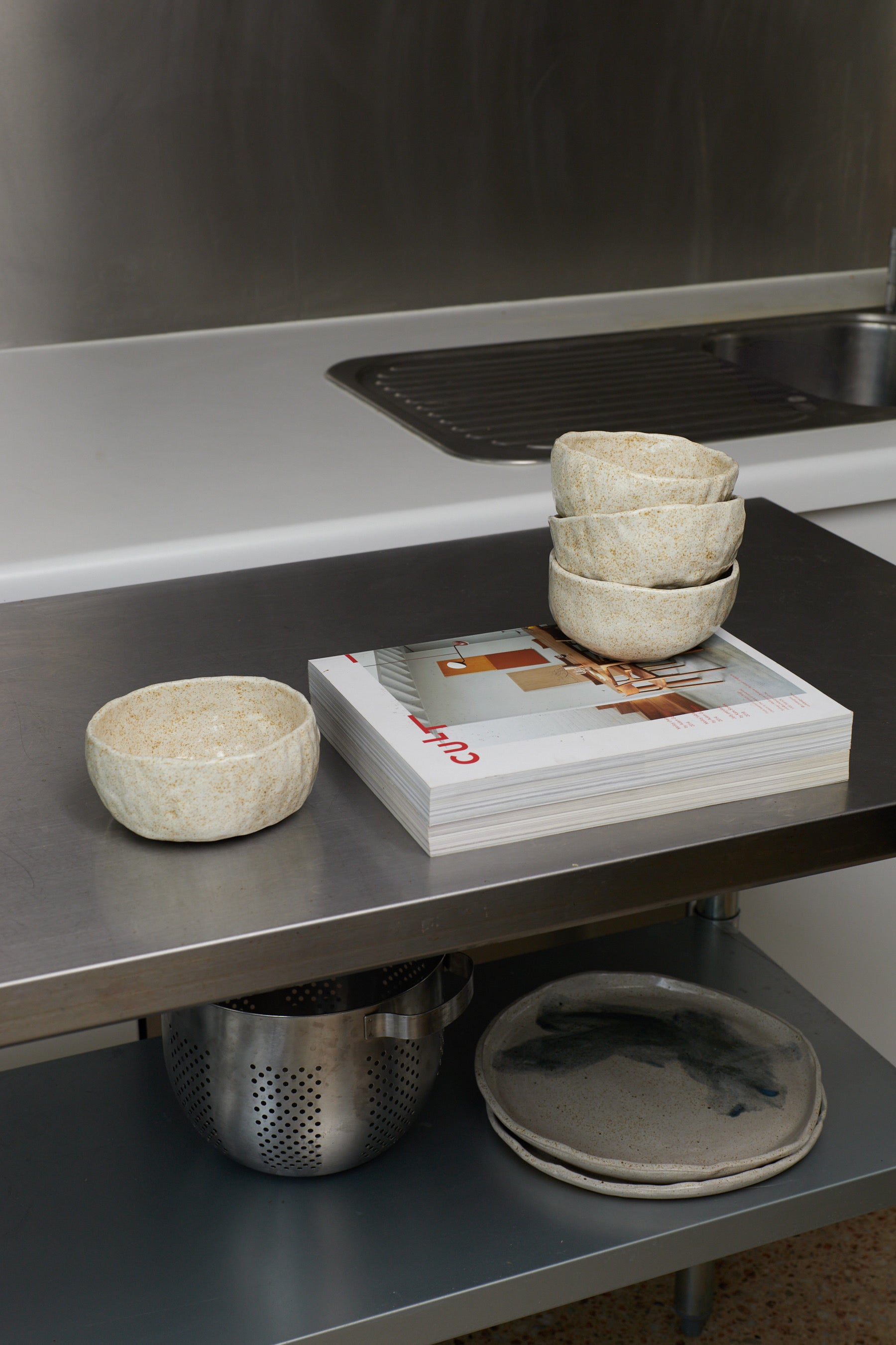 Kitchen counter with bowls, a magazine, and a colander.