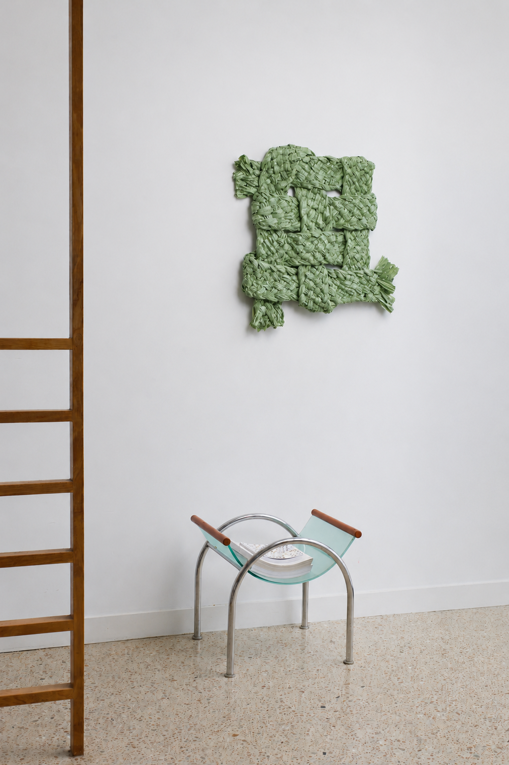 Green textured wall art piece on a white wall with a wooden ladder and glass chair in the foreground.