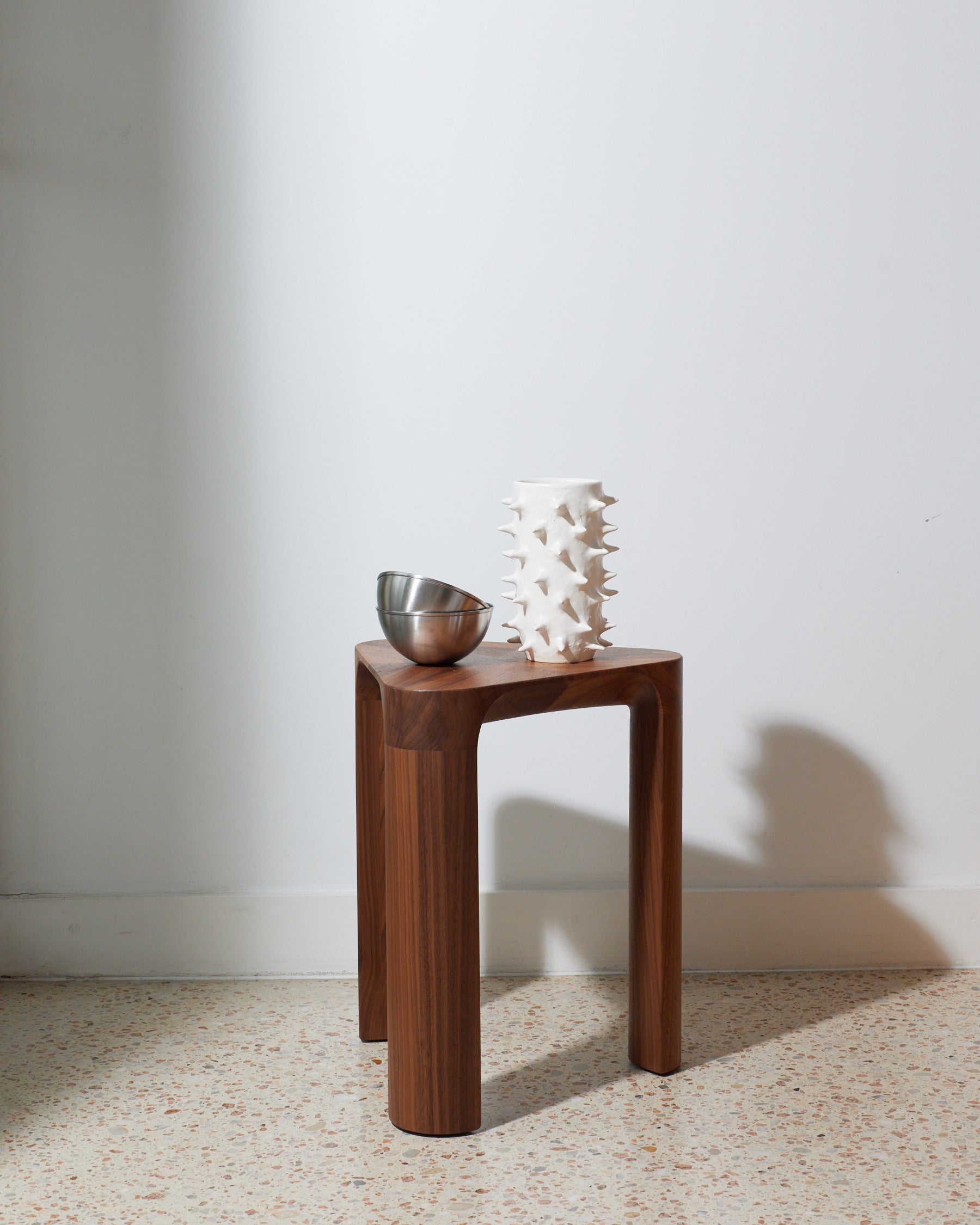 Wooden side table with a bowl and decorative piece against a white wall