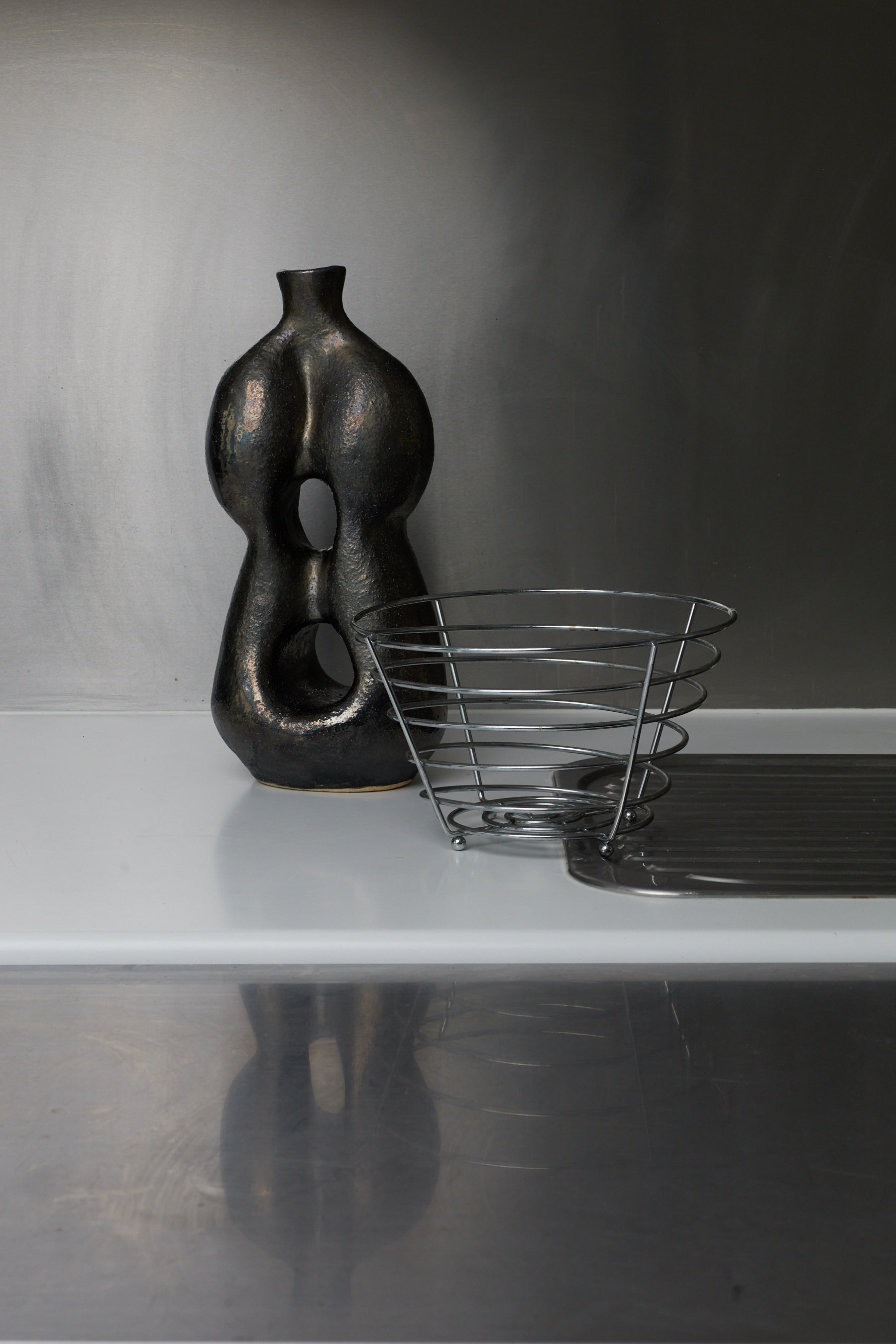 Black abstract vase and wire basket on a reflective surface with a dark background